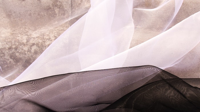 Translucent silk curtains in black and white lie on a beige tile floor.