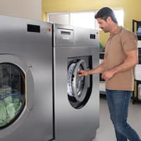 A laundry employee in a hotel comfortably closes the OneFingerTouch door of the Benchmark Performance Plus PWM 927 washing machine with one hand.