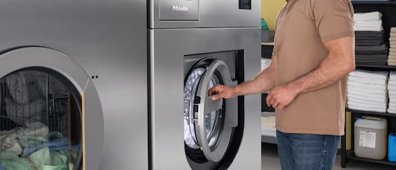 A laundry employee in a hotel comfortably closes the OneFingerTouch door of the Benchmark Performance Plus PWM 927 washing machine with one hand.