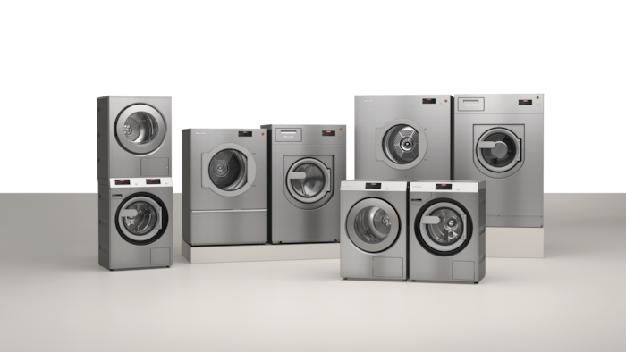 Die gewerblichen Performance Plus Waschmaschinen und Trockner der Benchmark Serie im Edelstahllook stehen als 3 Pärchen in einem Raum verteilt. Auf dem Bild sind Benchmark Industriewaschmaschinen und Trockner von 9 bis 28 kg Beladungskapazität zu sehen.