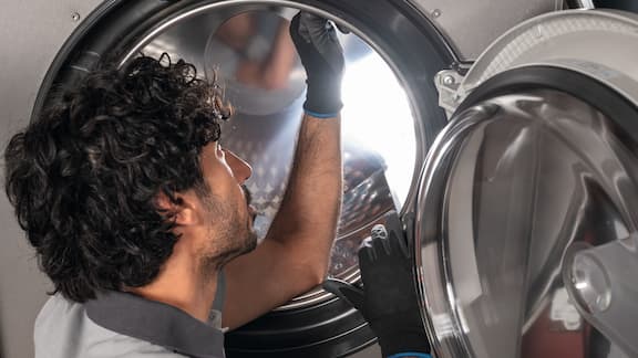 A person inspecting the drum of a professional Miele washing machine through the open door.