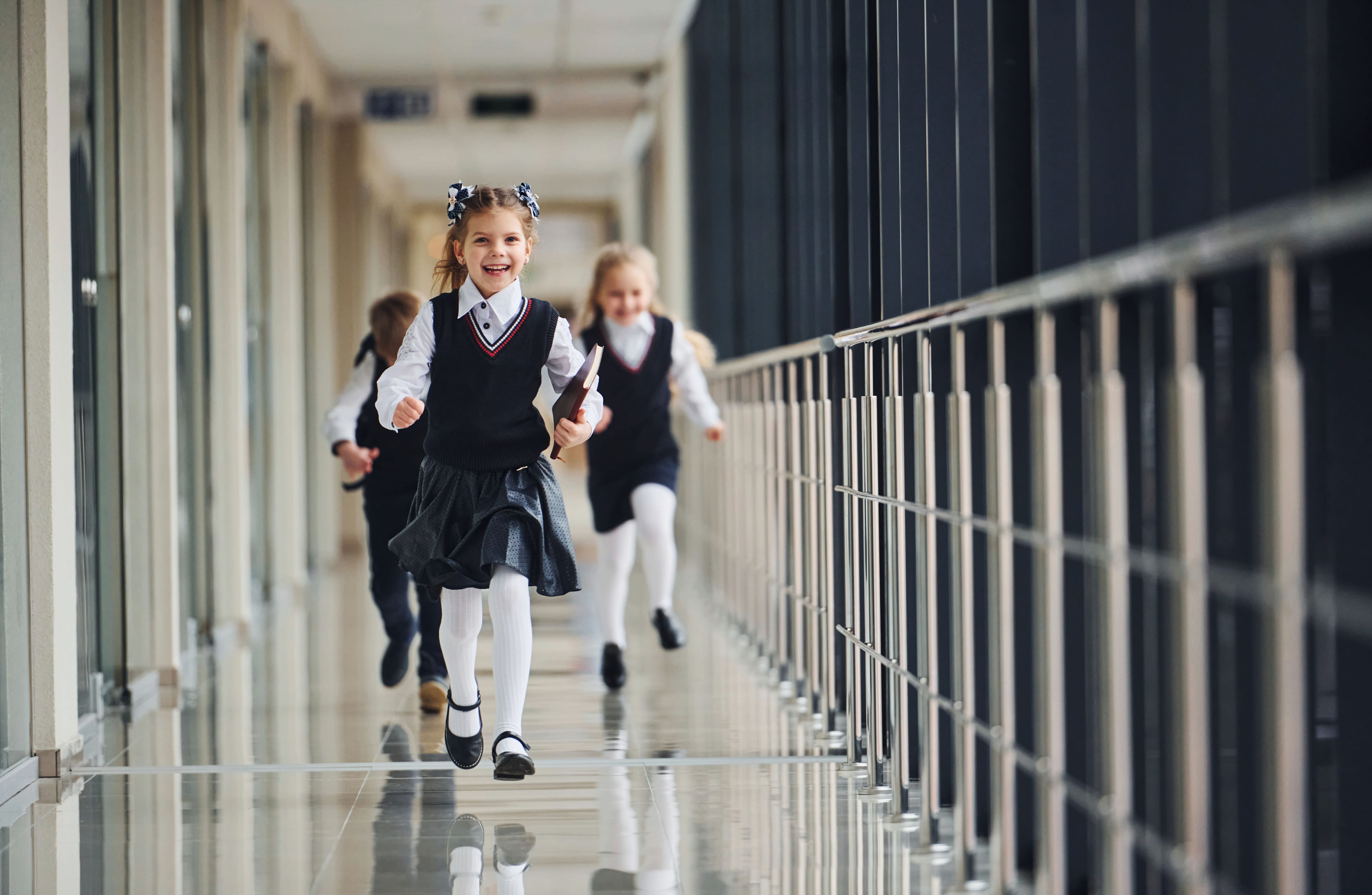 Zwei Kinder mit Schulranzen laufen fröhlich durch einen hellen Schulflur.