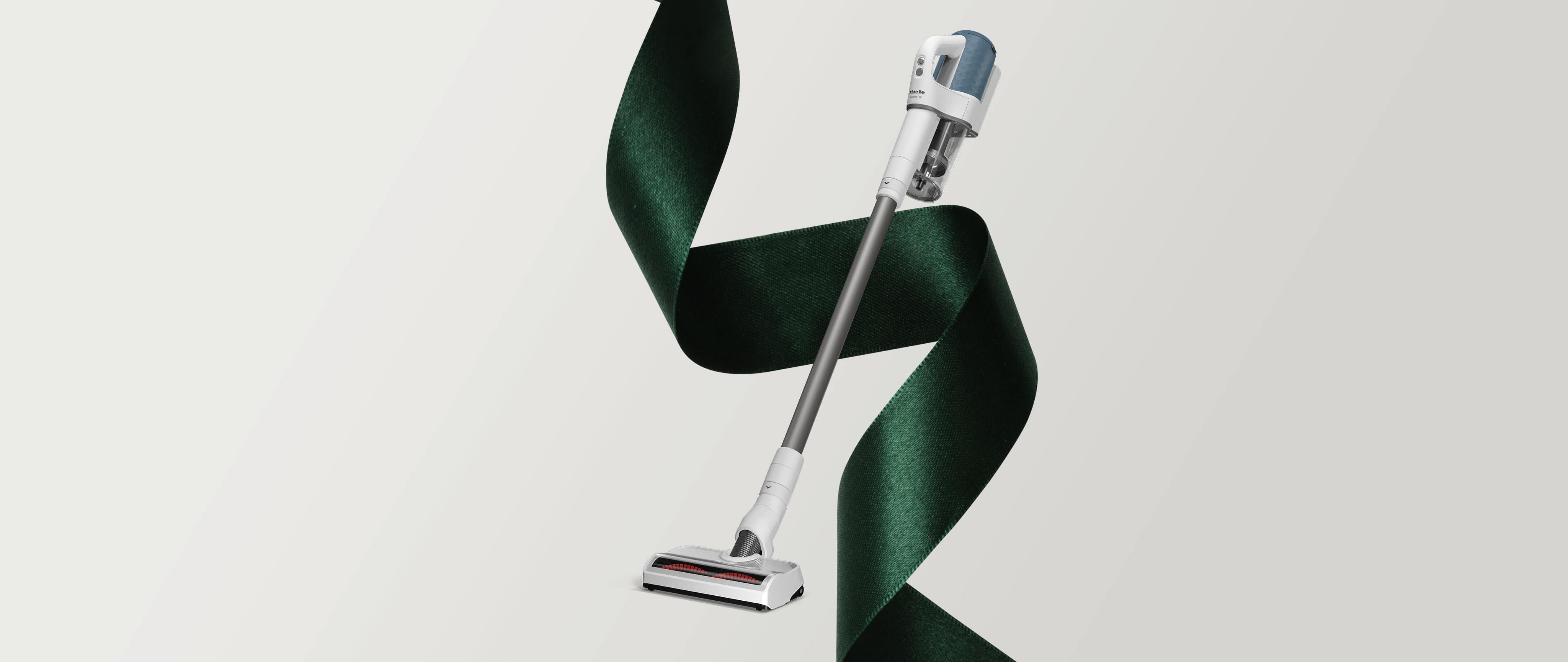 Grafika świąteczna z odkurzaczem pionowym Miele Duoflex ze świąteczną wstęgą do pakowania prezentów w tle Grafika świąteczna z odkurzaczem pionowym Miele Duoflex ze świąteczną wstęgą do pakowania prezentów w tle