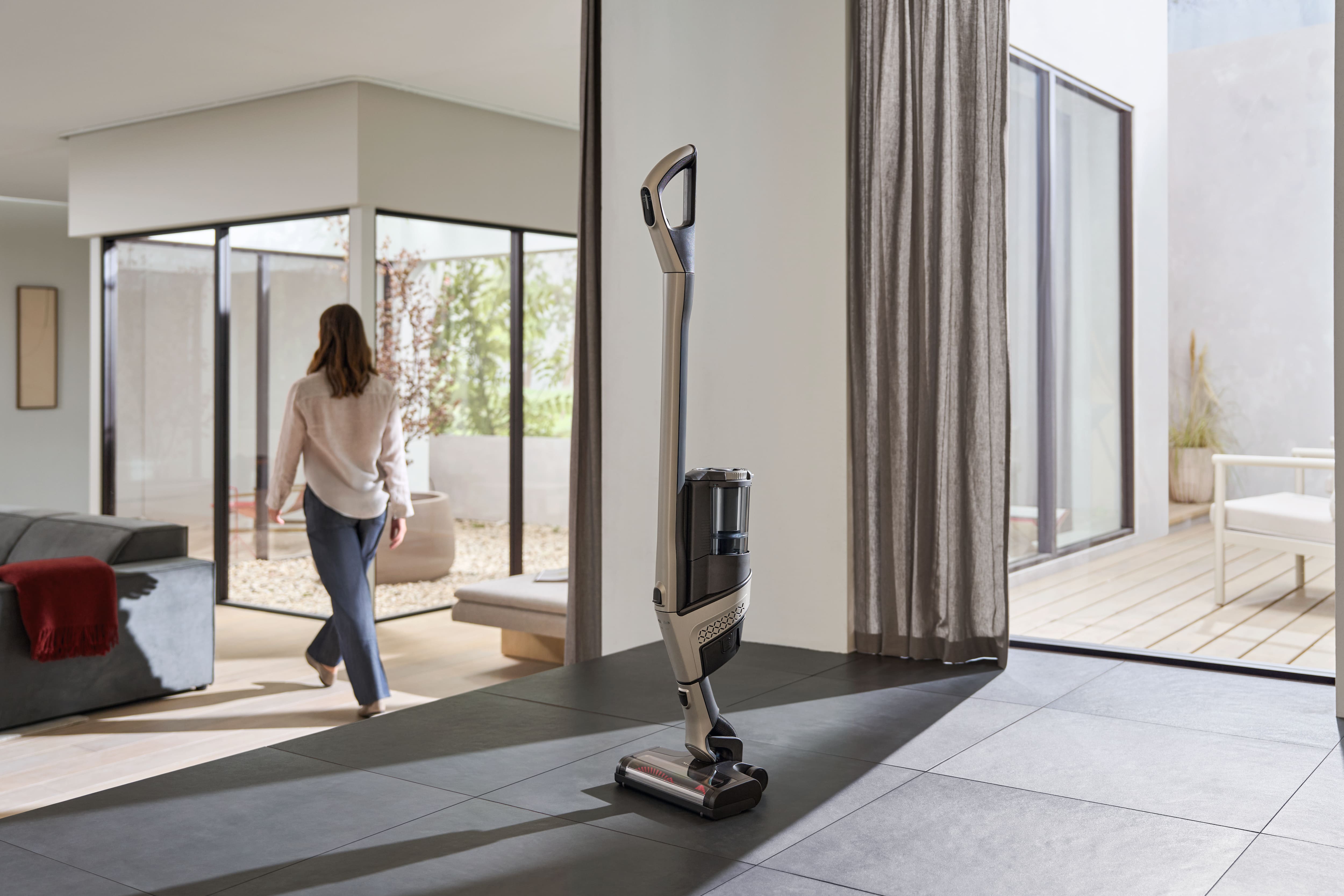 Stojący odkurzacz Miele Triflex HX3 w nowoczesnym pomieszczeniu i osoba, która zakończyła sprzątanie w tle
