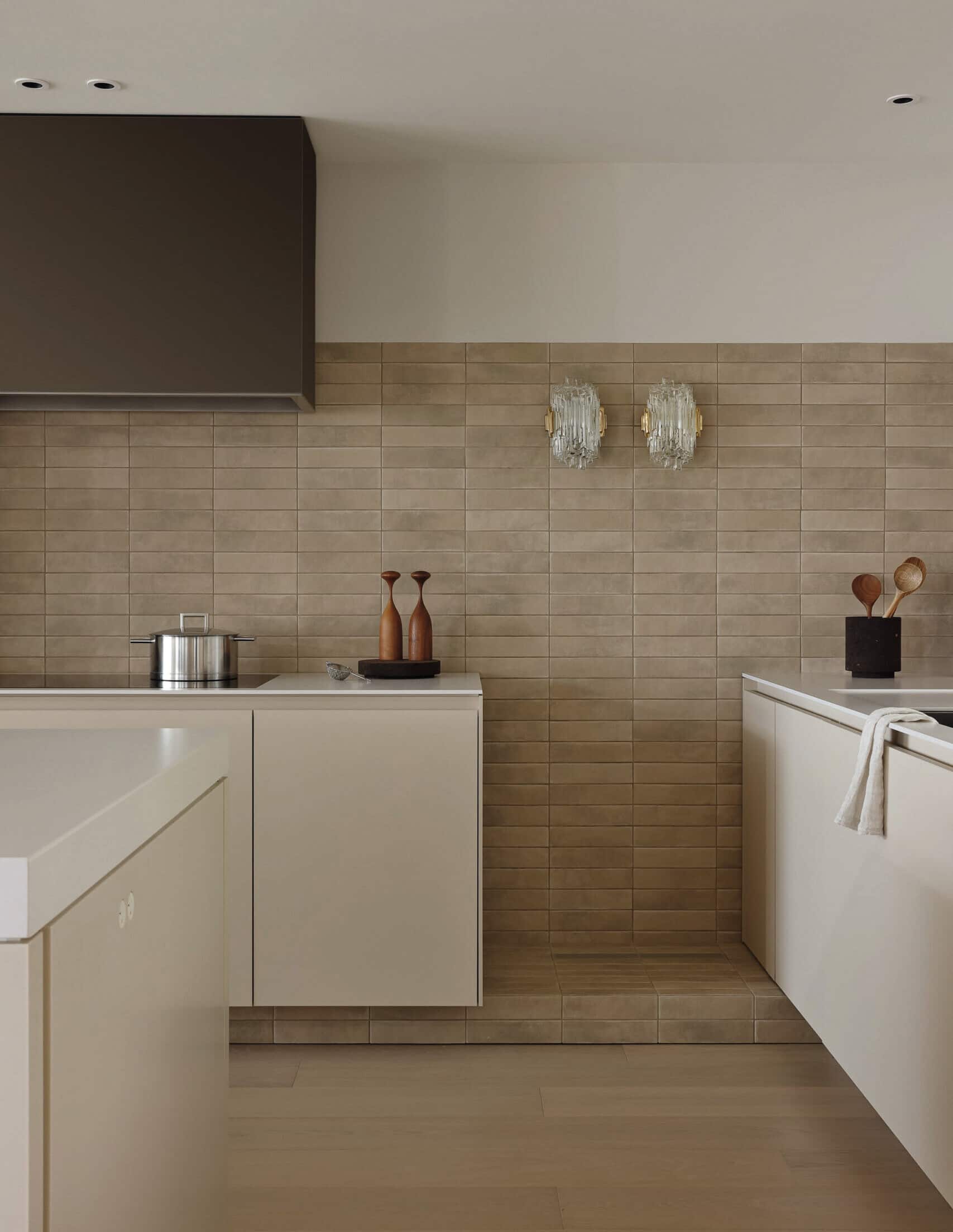 A minimalist kitchen corner with beige tile backsplash, light cabinetry, and modern wall sconces.