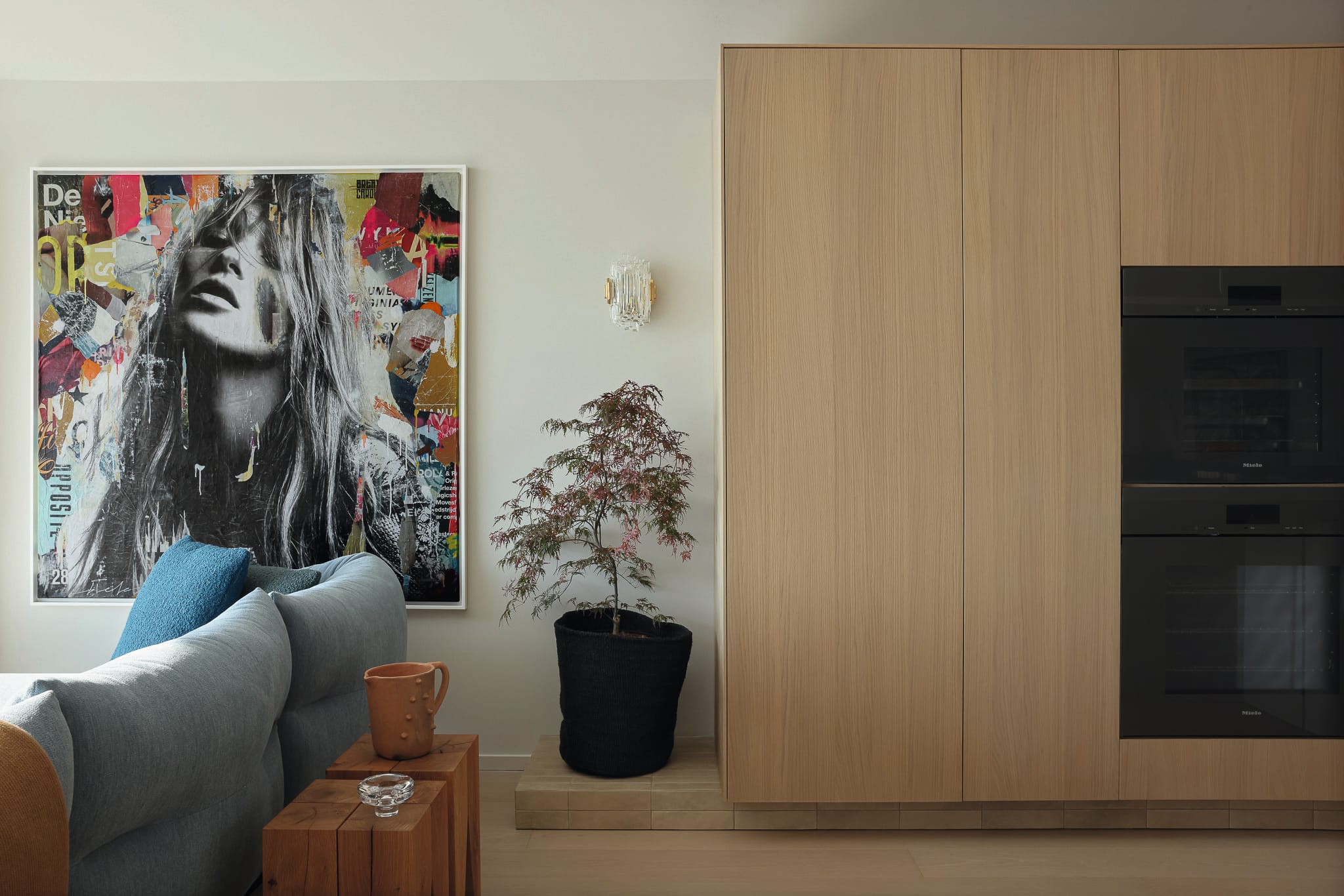 modern living space with light wood cabinetry, a large art piece, and a potted plant beside a sofa.