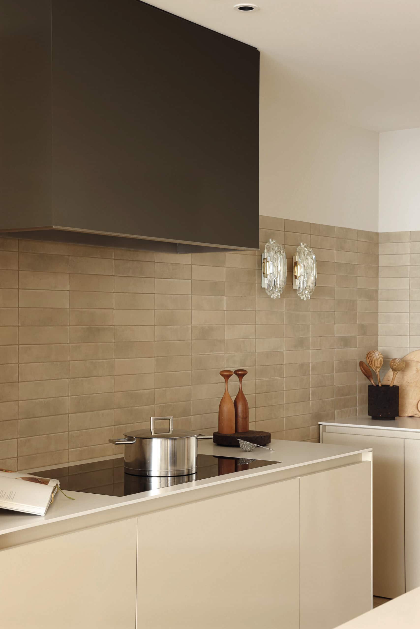 A modern kitchen counter with beige cabinetry, a tiled backsplash, and a large dark range hood above a pot.