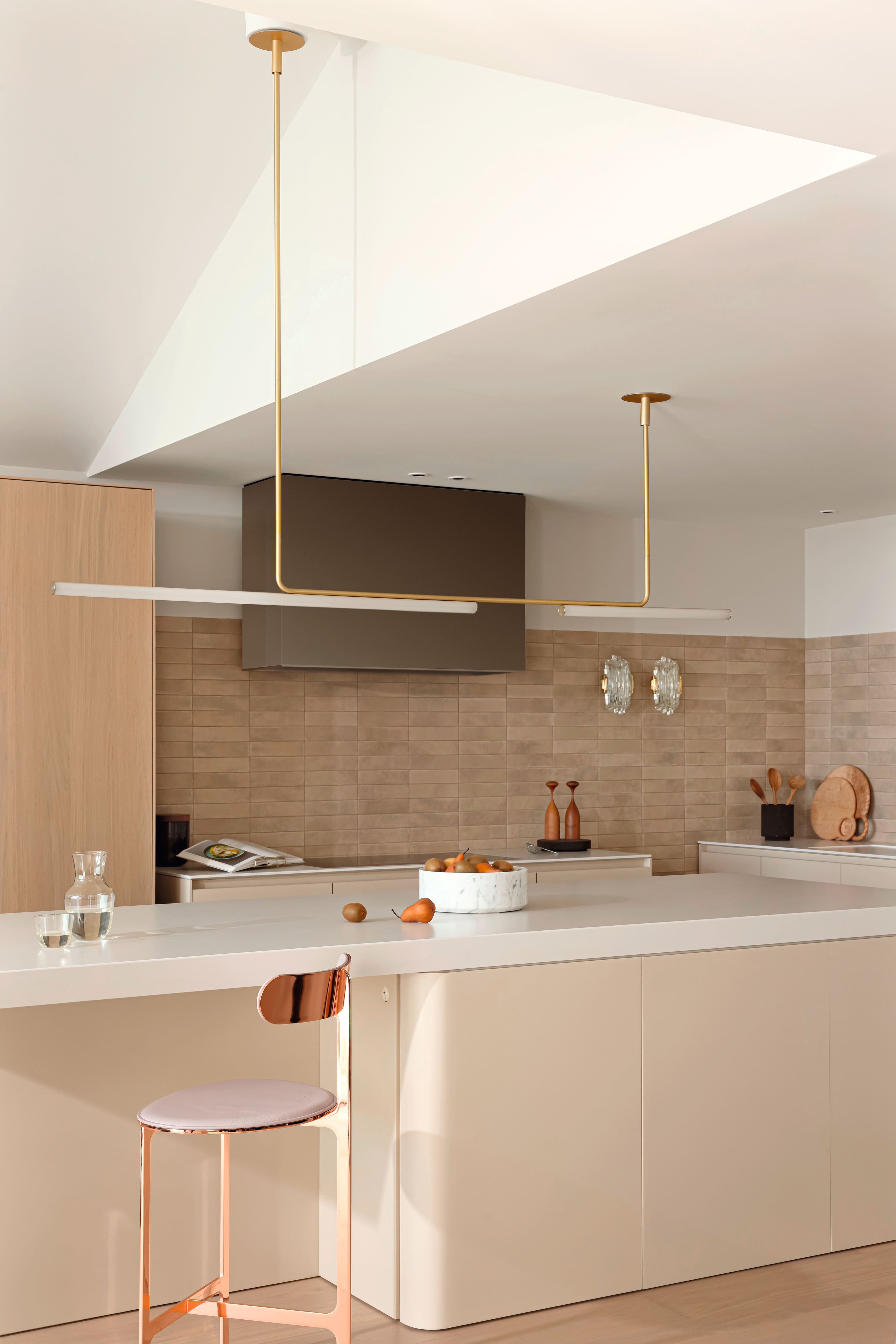 A bright modern kitchen with a large island, beige cabinetry, and slim gold pendant lights.