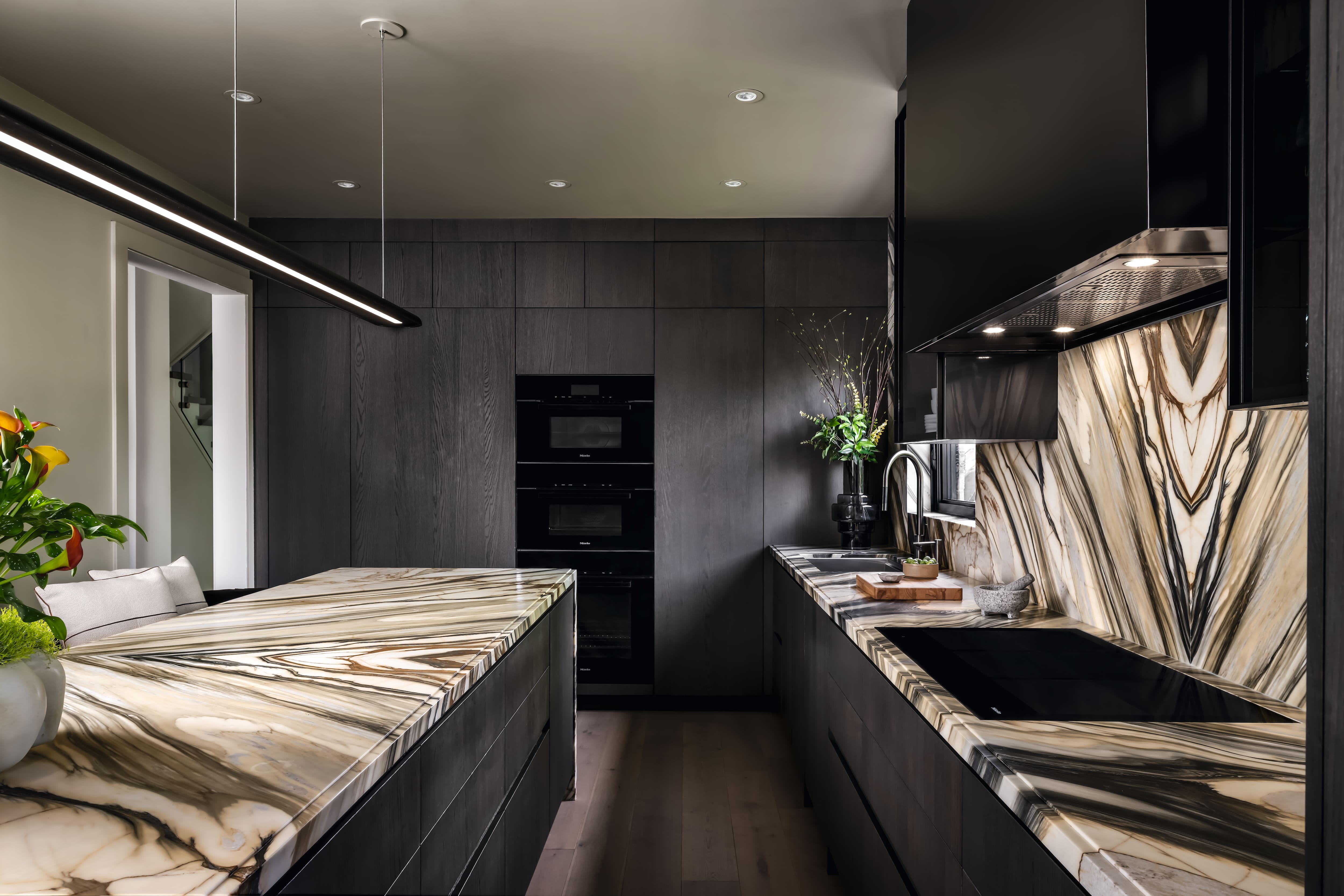 A modern kitchen with dark cabinetry and dramatic marble surfaces surrounding the island and cooktop.