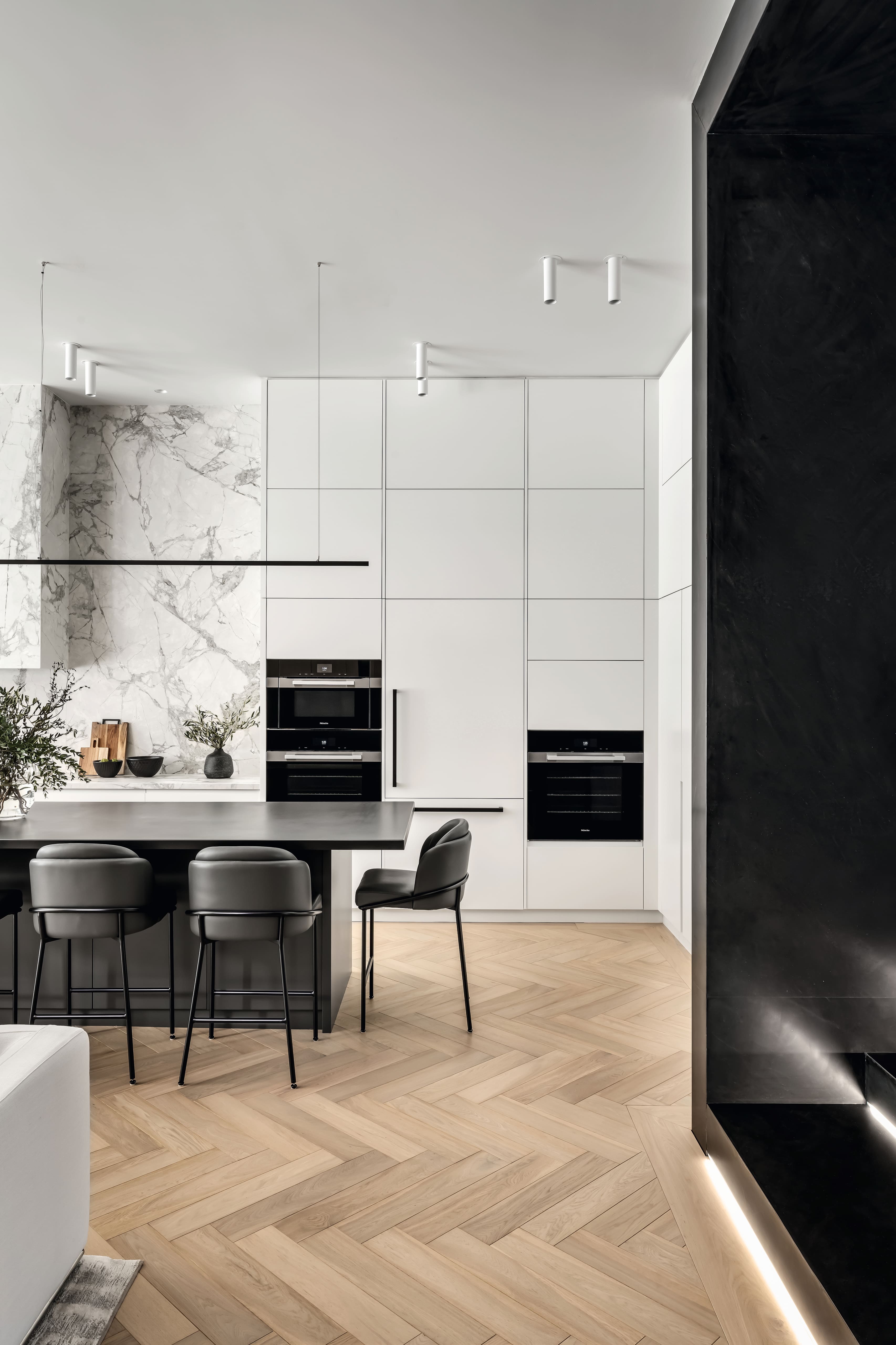 A modern kitchen with white paneled cabinetry, a marble backsplash, and dark island seating.