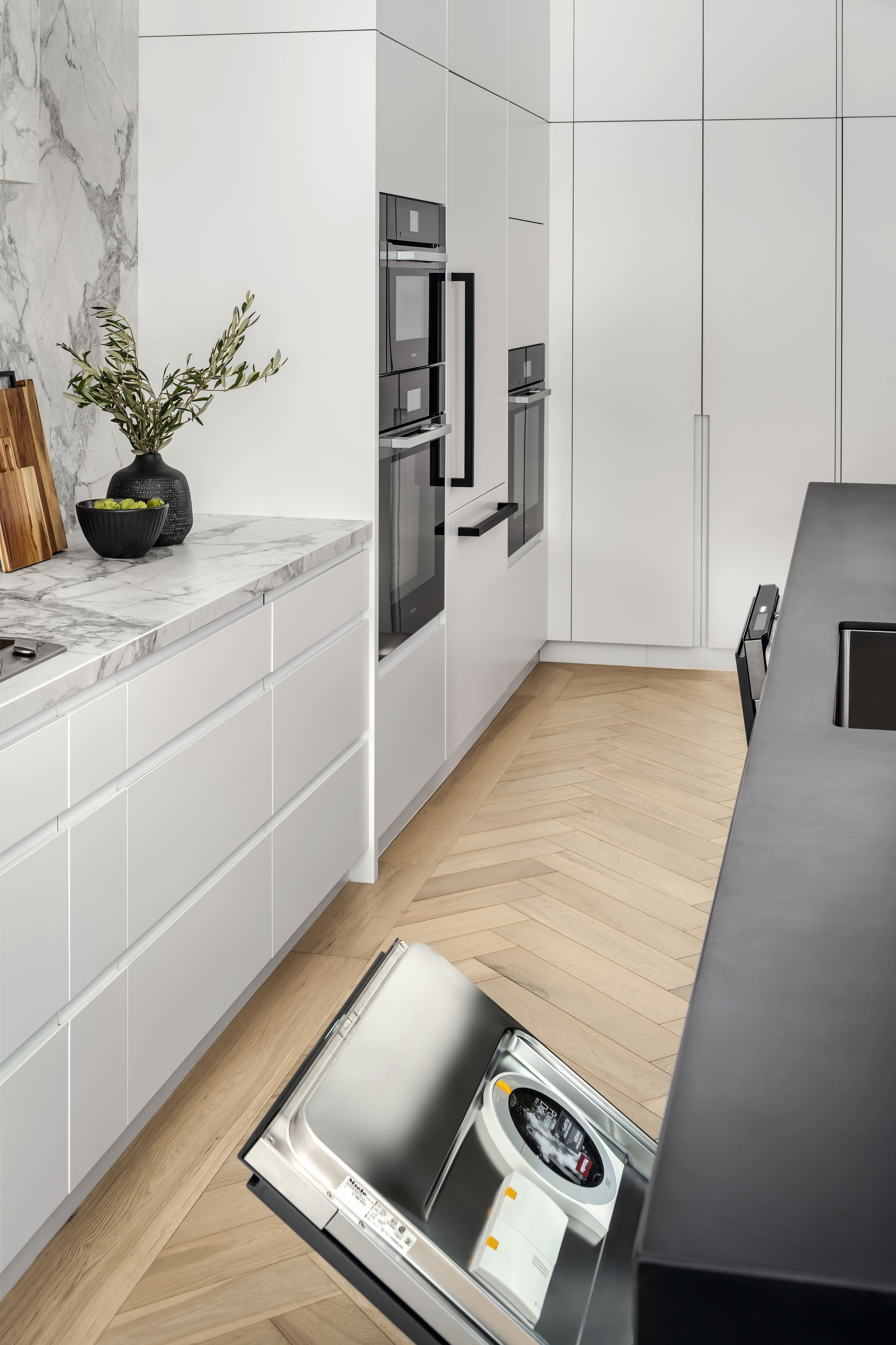 A modern kitchen scene with an open built-in dishwasher next to sleek white cabinetry and marble countertops.