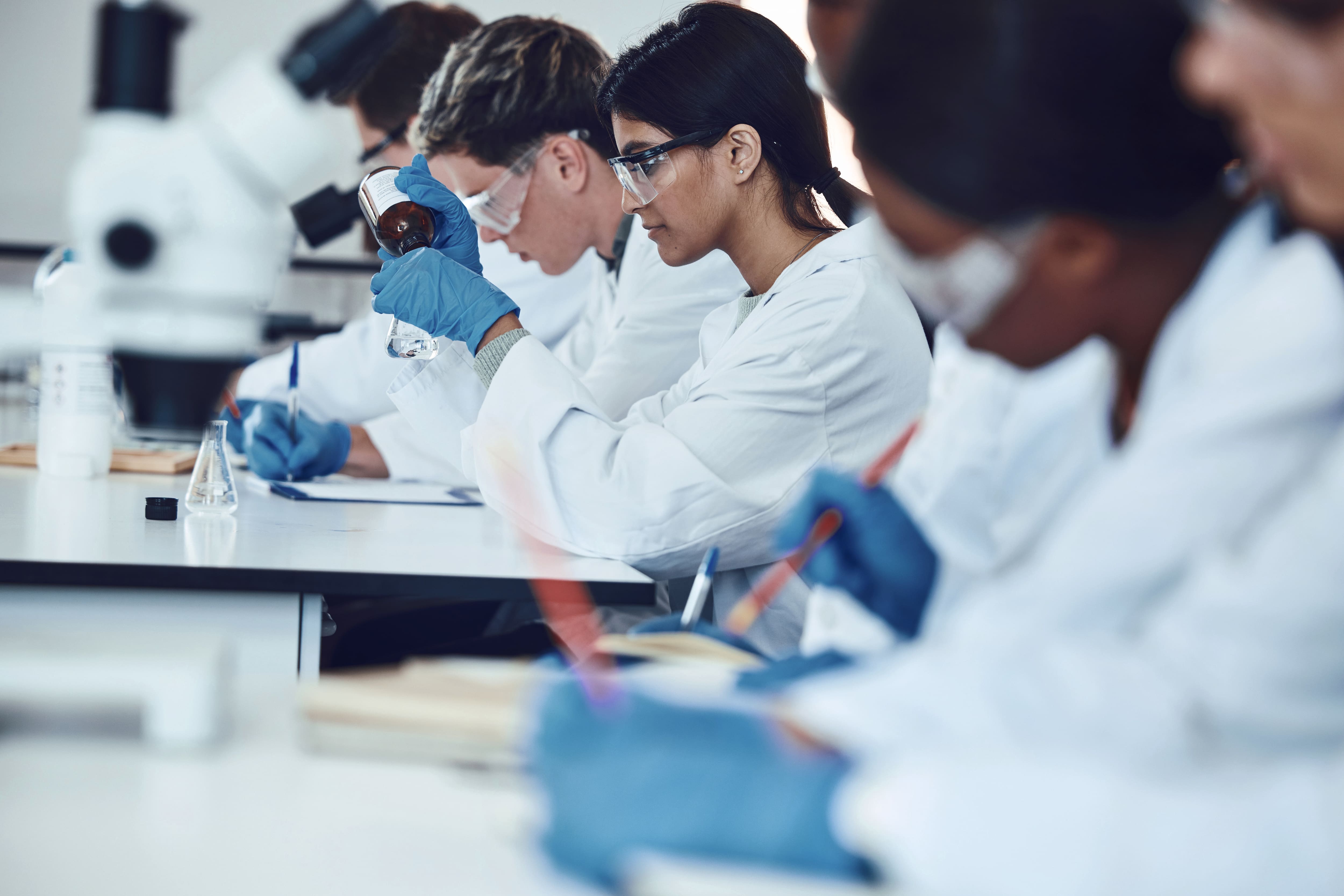 StudentInnen in Laborkitteln führen konzentriert ein Experiment im naturwissenschaftlichen Labor durch.