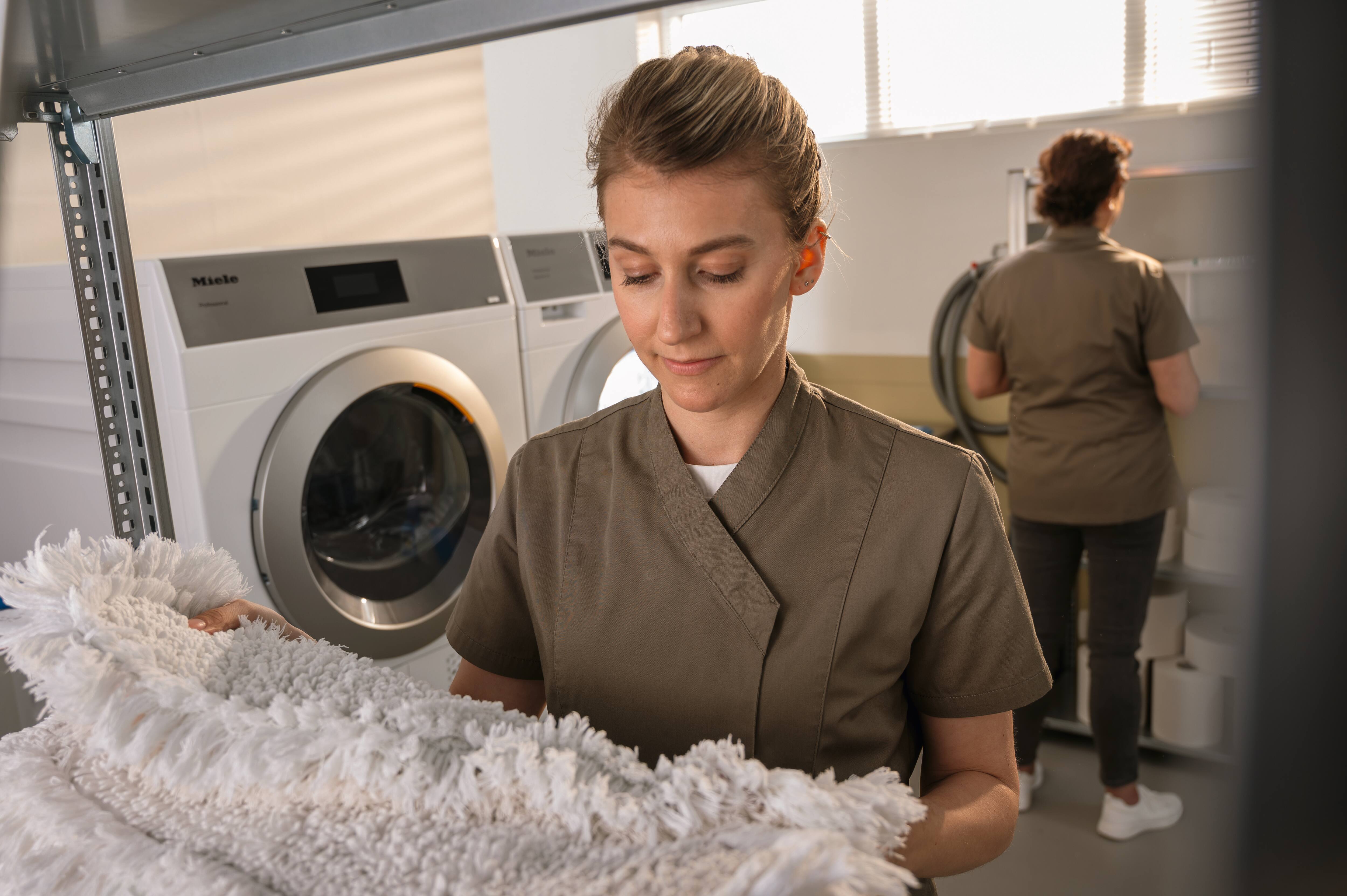 Miele Little Giants machines in a laundry setting with one door open and grey mop heads in front of them.