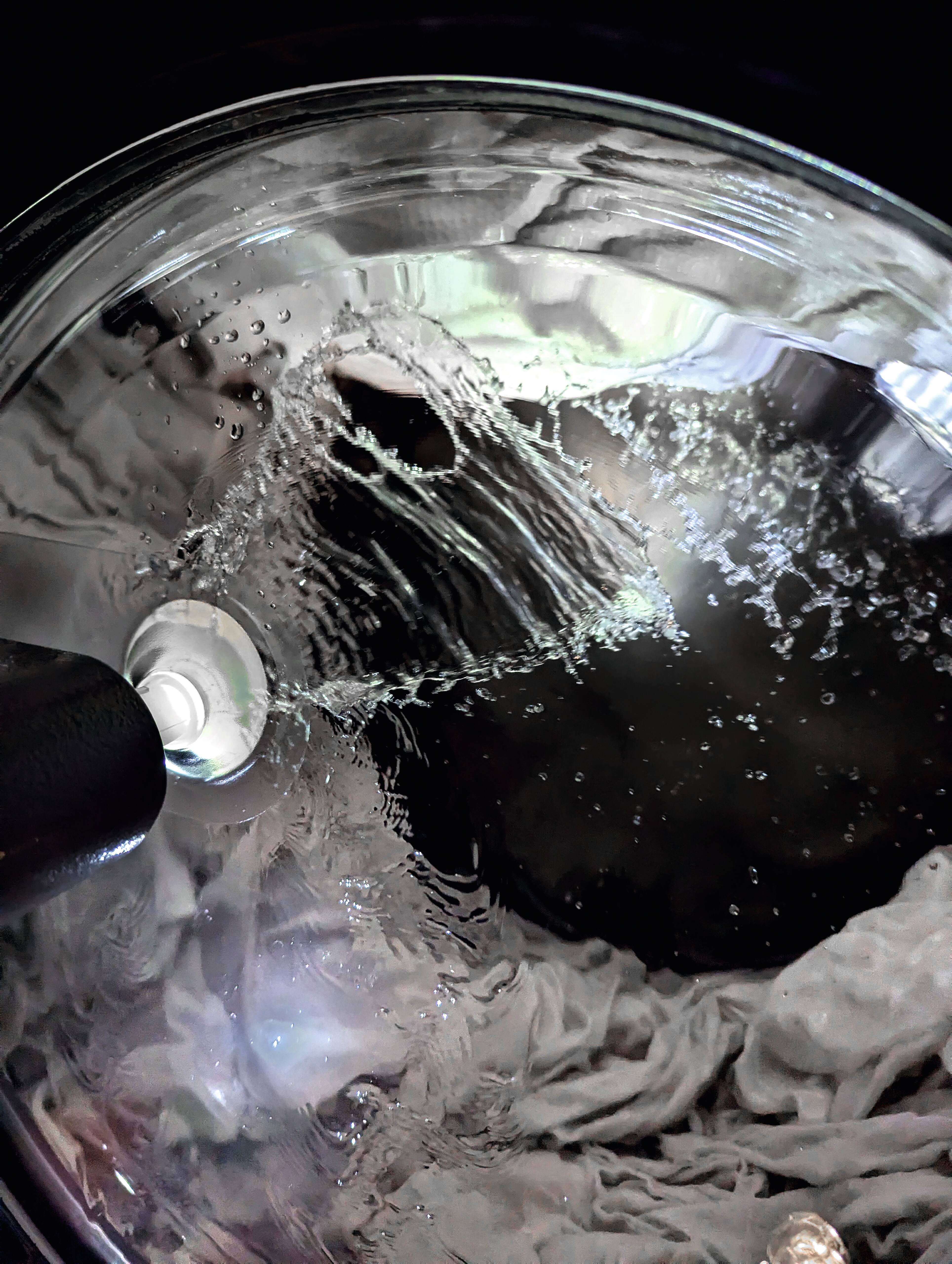 Nahaufnahme der Tür der Benchmark PWM 920 PWP Waschmaschine. Der Blick geht von außen durch die Tür in die Trommel. Man sieht einen Wasserstrahl der von der Innenseite des Türgriffs in die Waschmaschinentrommel geht.