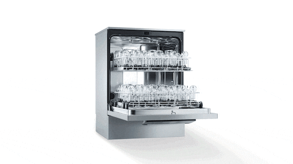 A laboratory washer loaded with very large laboratory glassware and measuring cylinders. A lab technician is holding another measuring cylinder in her hand.